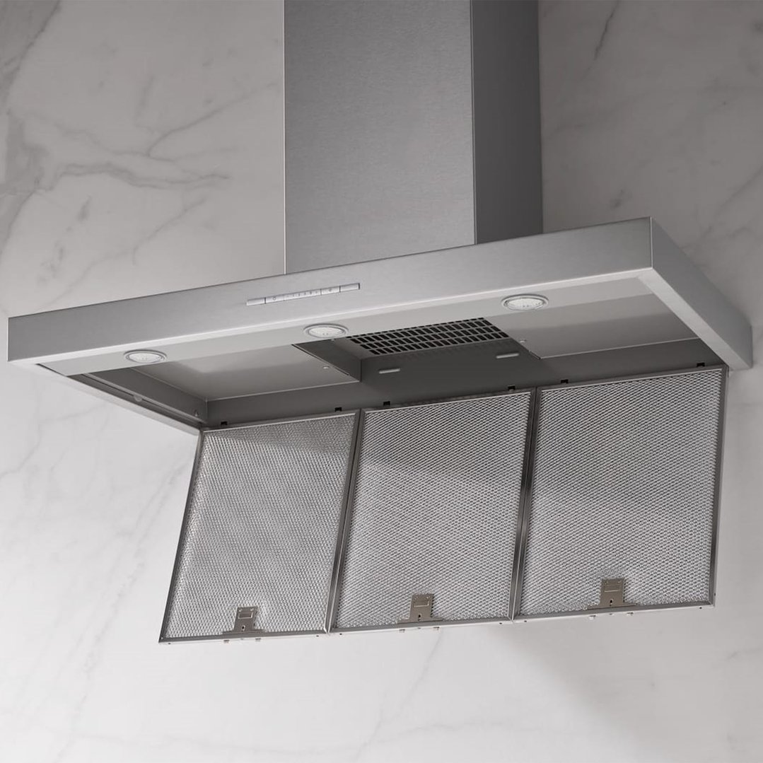 Stainless steel range hood with mesh filters and lights against a marble wall