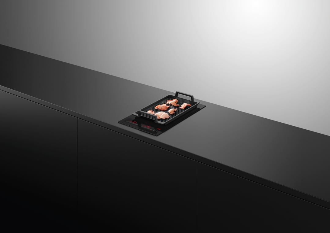 Induction cooktop with a grill pan cooking food, integrated into a dark kitchen counter