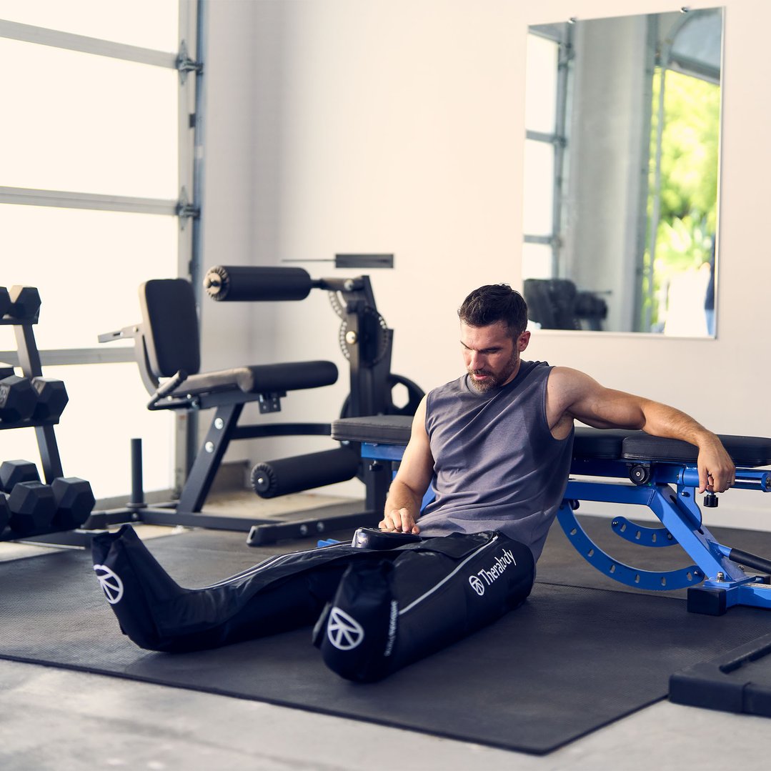 Man sitting on gym floor wearing JetBoots Prime massager in a home gym