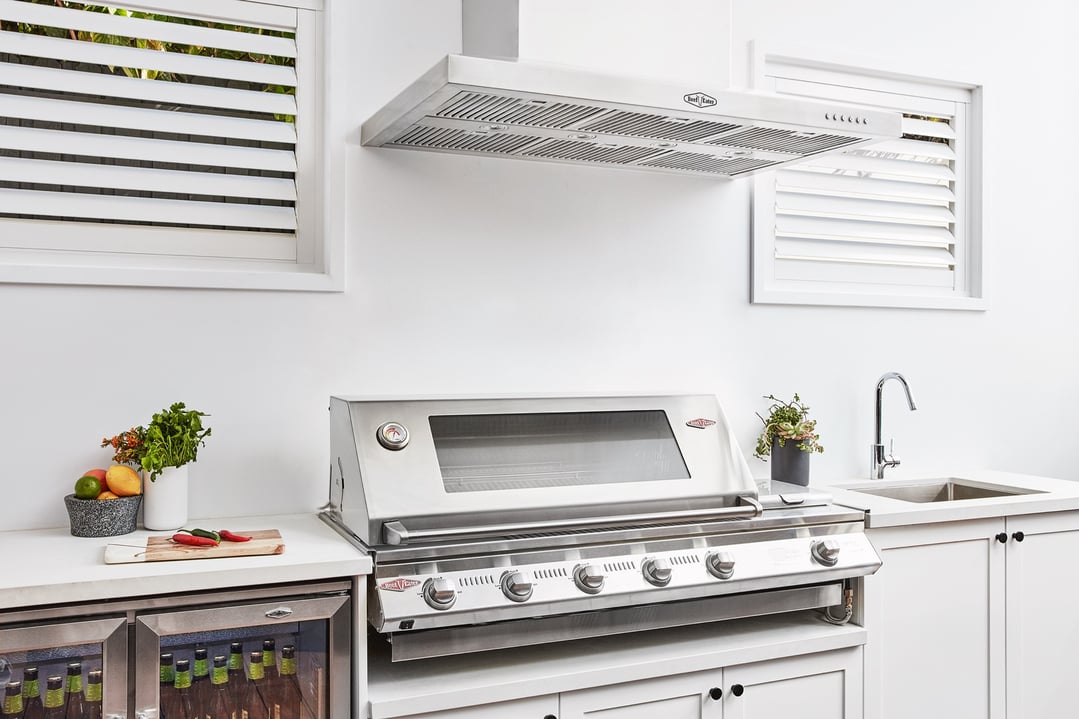 Stainless steel outdoor canopy hood above a barbecue grill in an outdoor kitchen