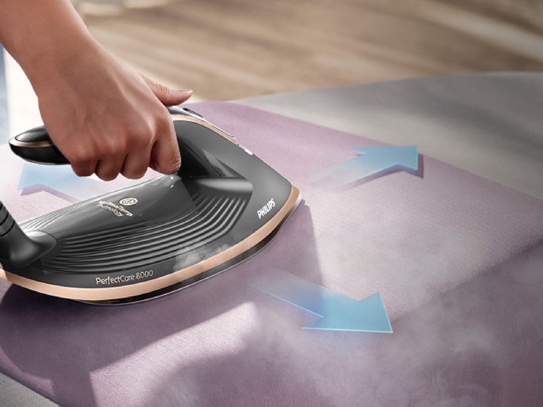 Hand holding a Philips PerfectCare Steam Generator 8000 Series iron on an ironing board