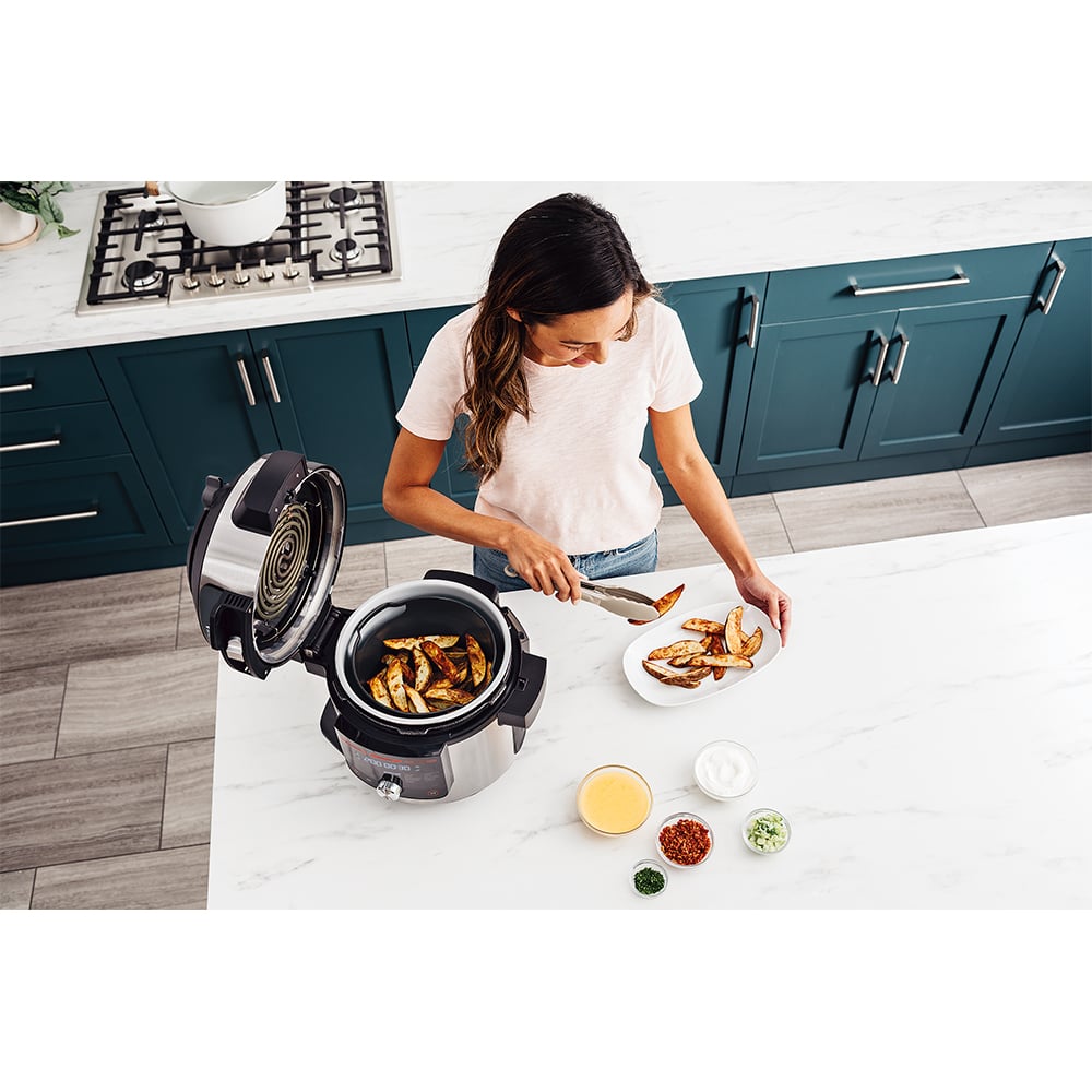 Woman using tongs to transfer potato wedges from a multicooker to a plate
