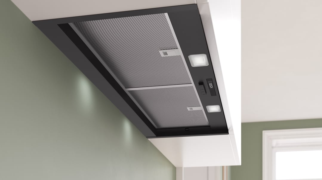 Integrated rangehood with mesh filters and controls, installed in a kitchen with green walls