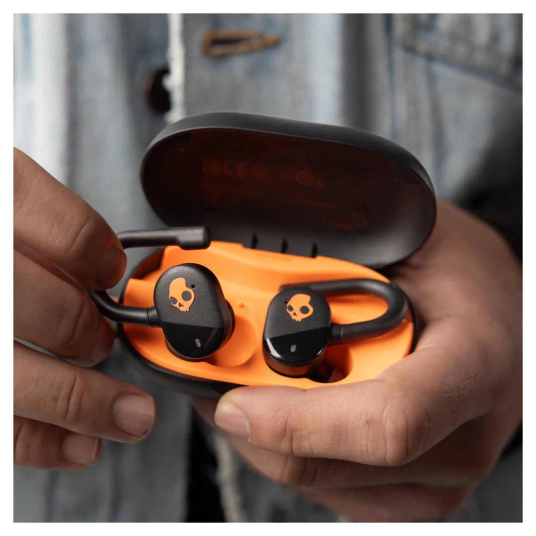 Hands holding black and orange Skullcandy Push Play Active TWS headphones in case