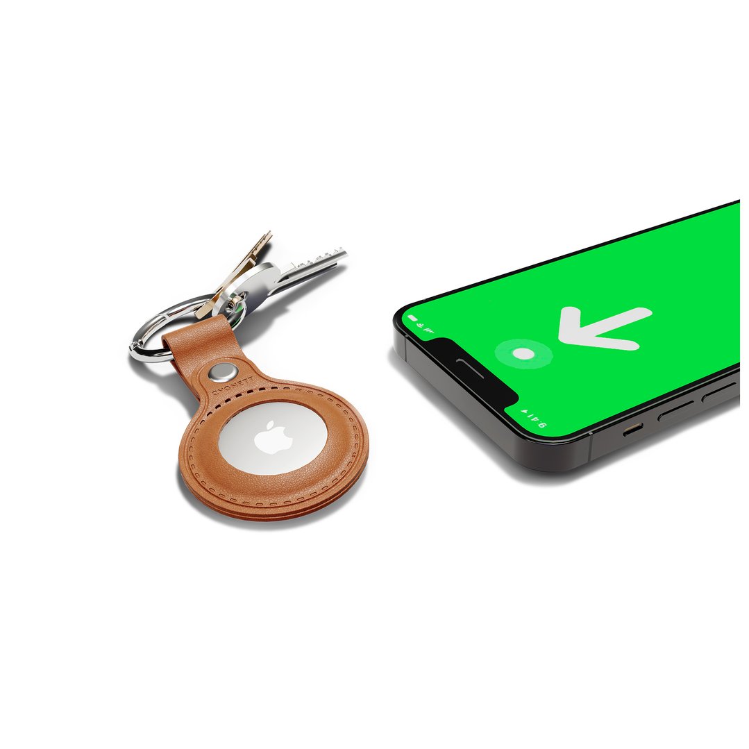 Tan leather AirTag case with keys next to a smartphone displaying a green screen