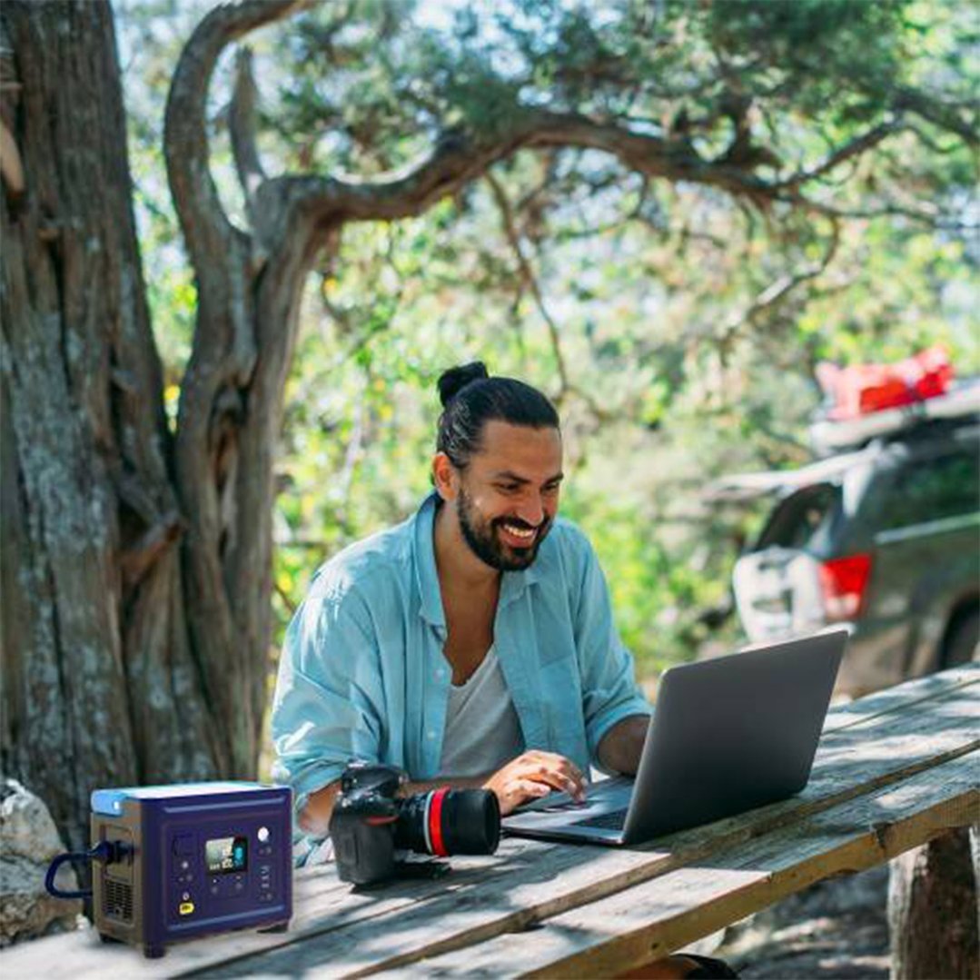 Man using a laptop and portable power station on a wooden picnic table outdoors