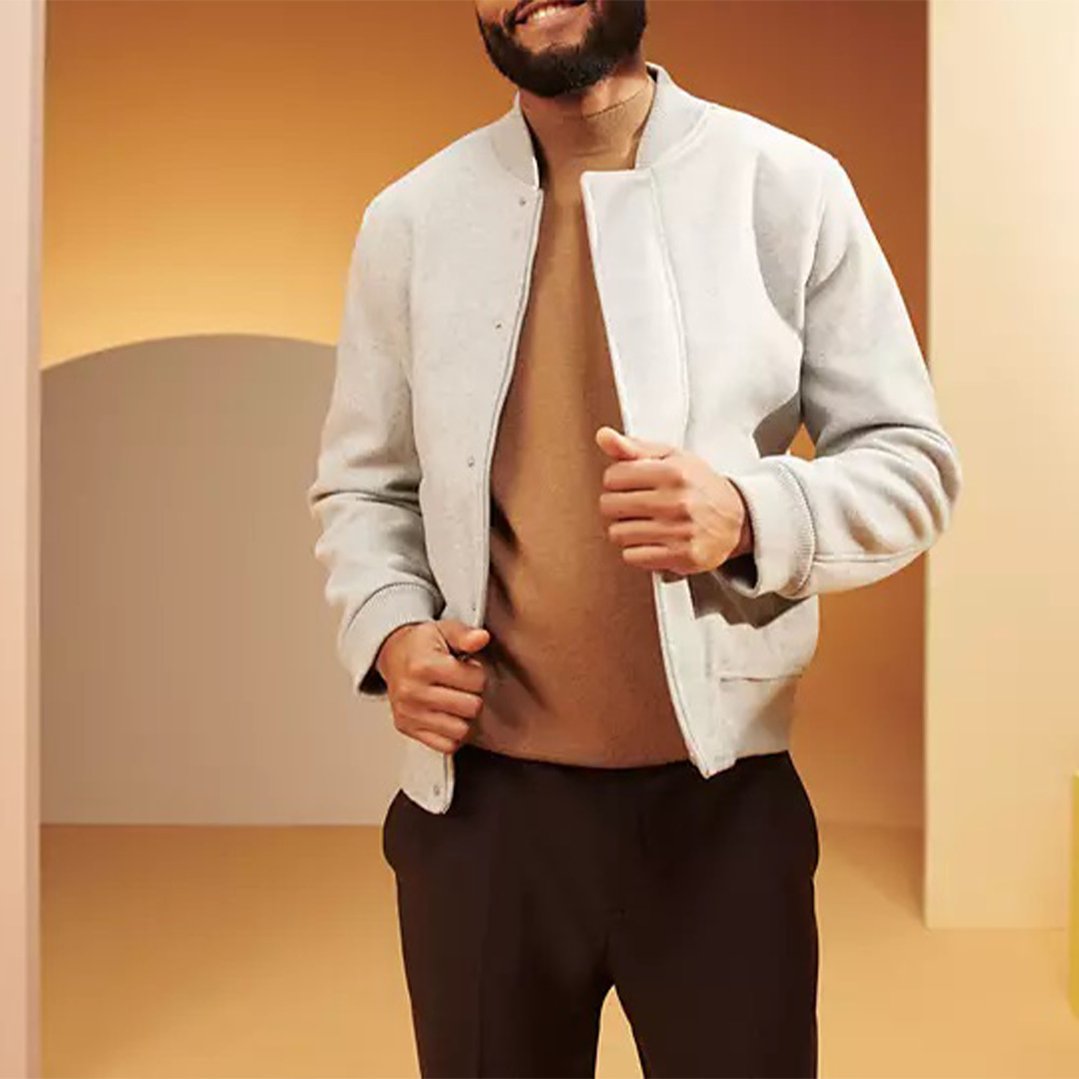 Man wearing a light grey jacket and brown shirt in a warm-toned room