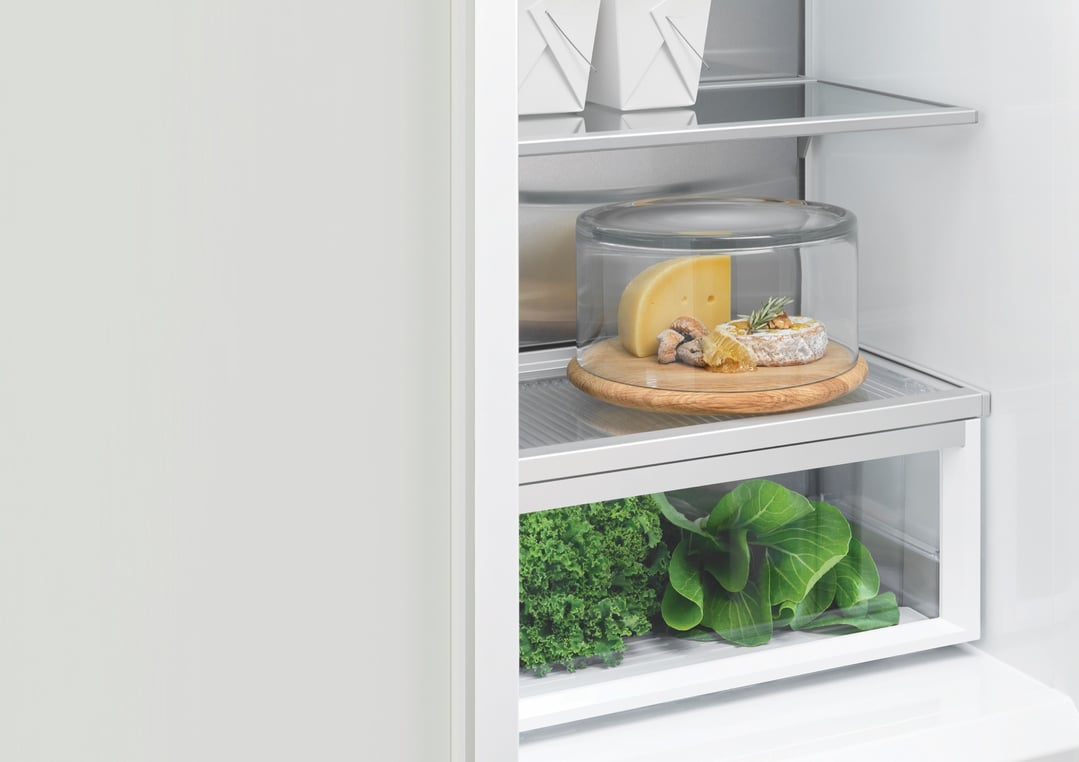 Open integrated dual zone refrigerator showing cheese and fresh greens on shelves