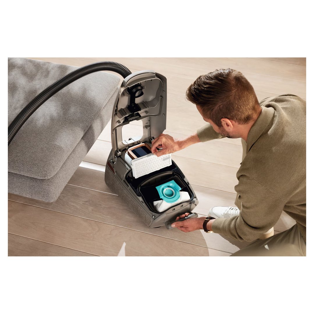 Man inserting a HEPA AirClean filter into a vacuum cleaner on a wooden floor