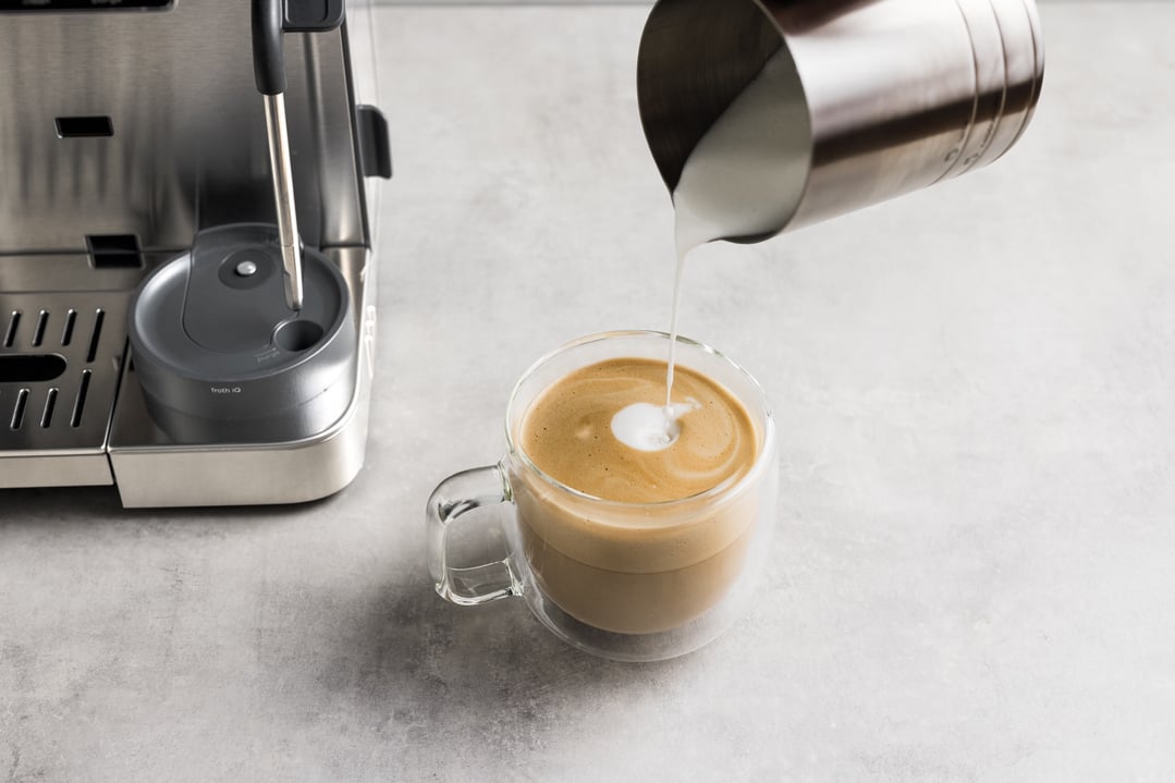 Pouring frothed milk into a glass mug of coffee from a NINJA coffee machine