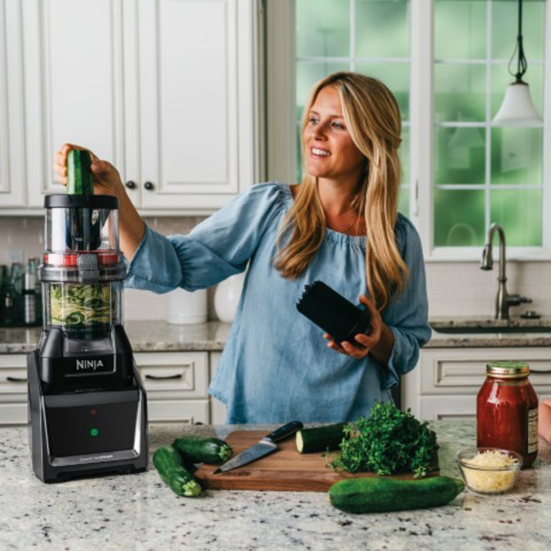 Woman using a Ninja blender to spiralize zucchini in a kitchen