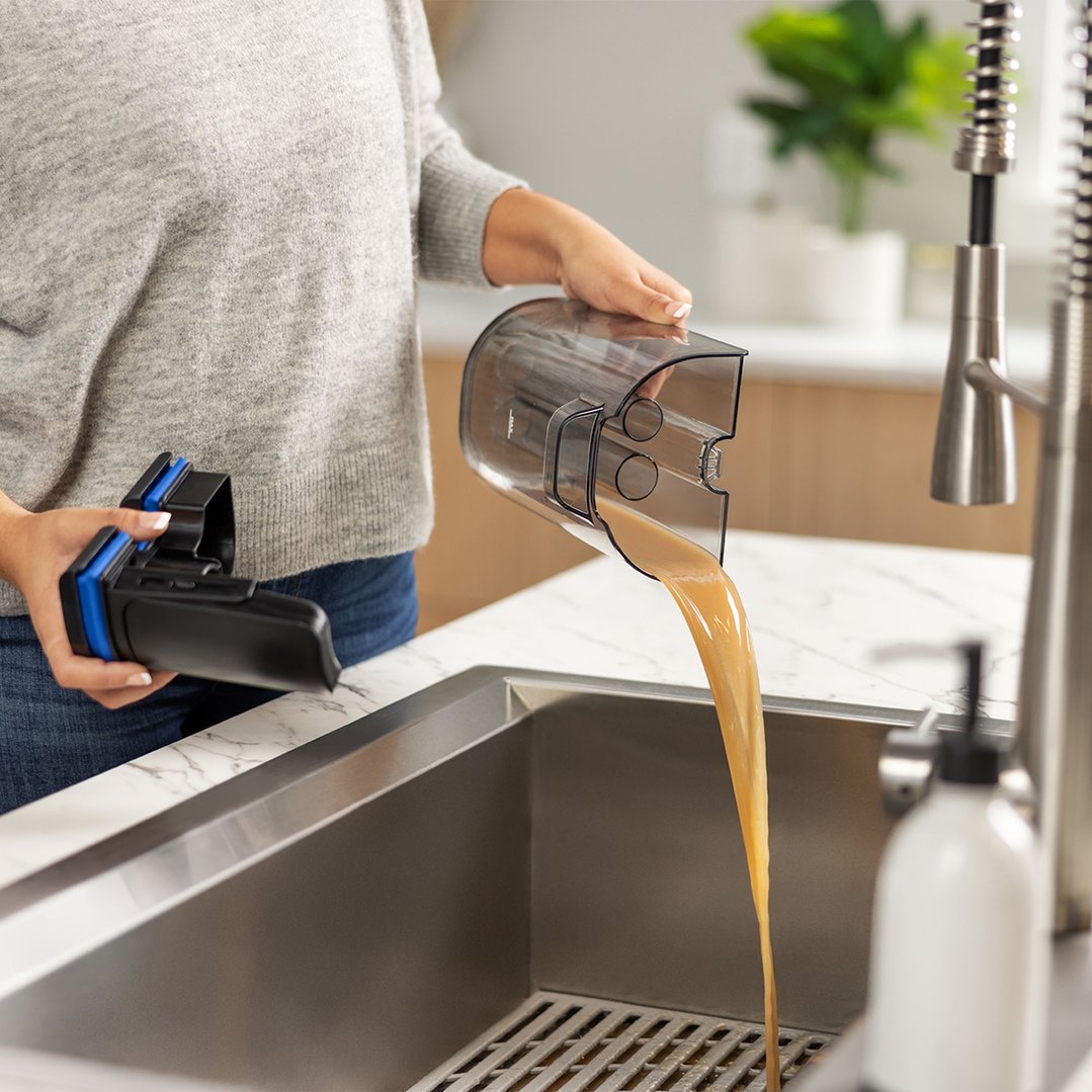 Person emptying dirty water from a vacuum cleaner tank into a kitchen sink