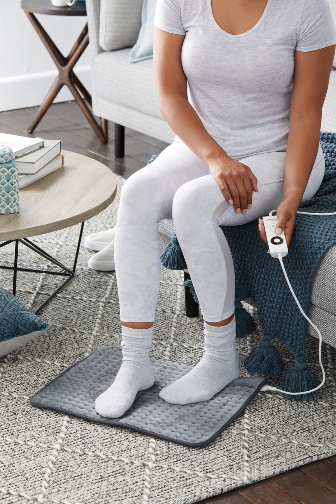 Woman sitting on sofa with feet on a heating pad