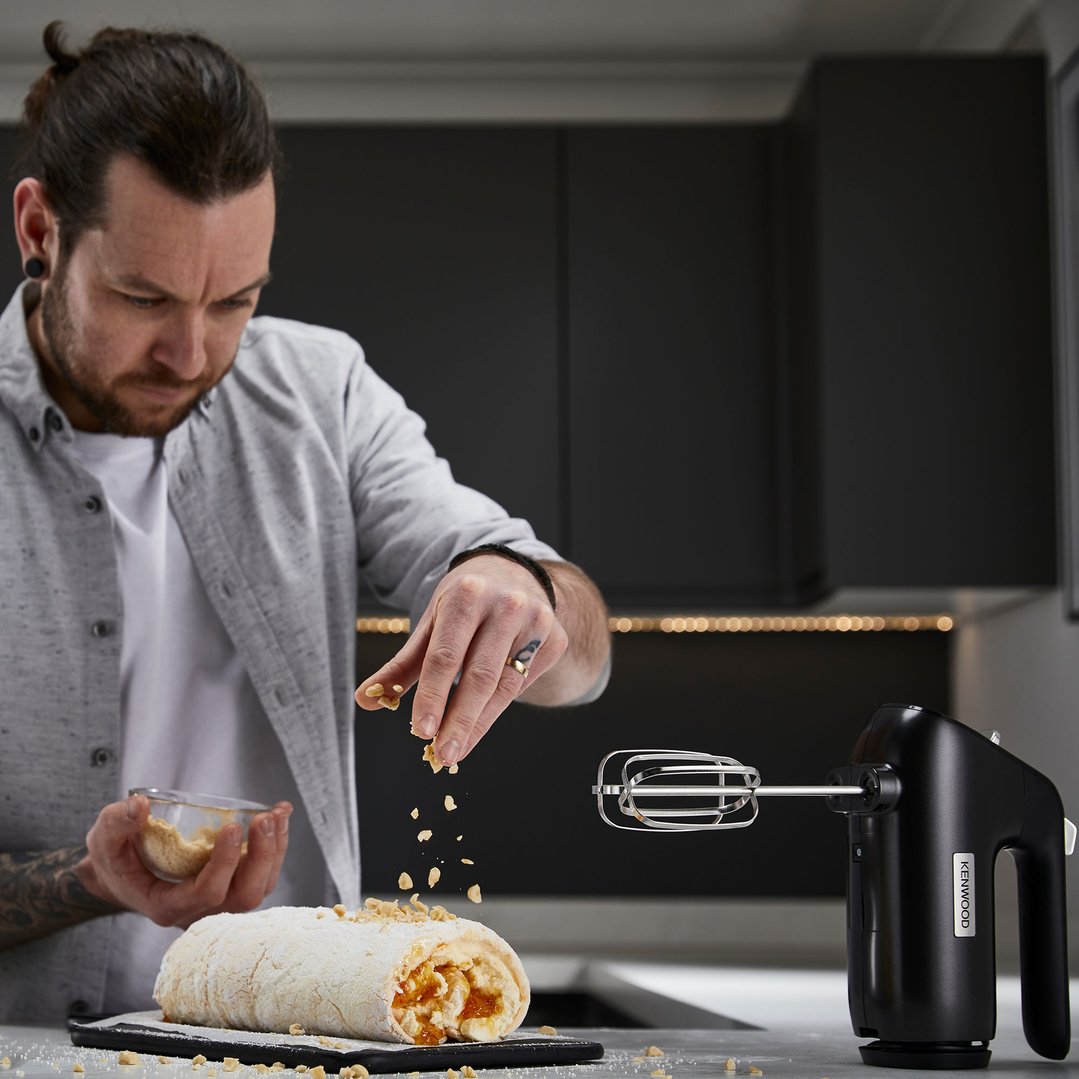 Man sprinkling nuts on a meringue roll with a KENWOOD hand mixer nearby