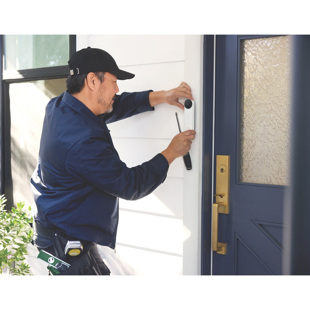 Man installing a Nest Doorbell on a white wall next to a blue door