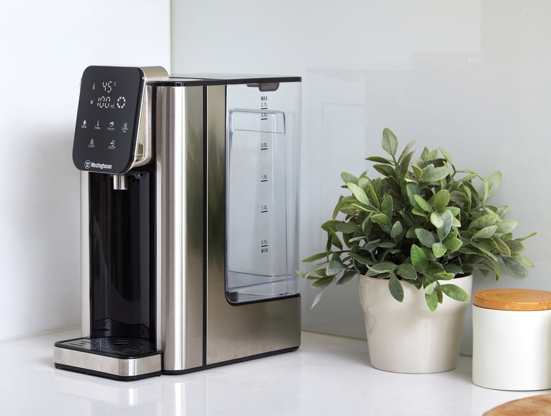 Instant hot water dispenser on a white countertop next to a potted plant