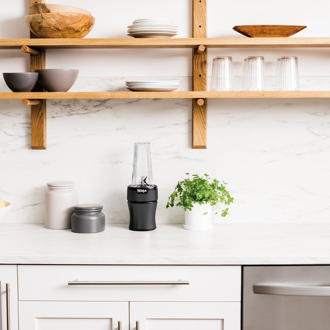 Black Ninja blender on a kitchen counter with shelves and decor