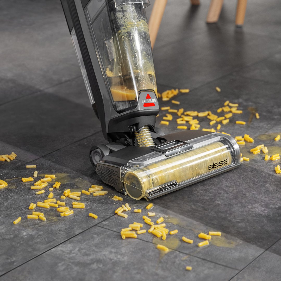 Bissell vacuum cleaner cleaning spilled macaroni and cheese on a dark floor