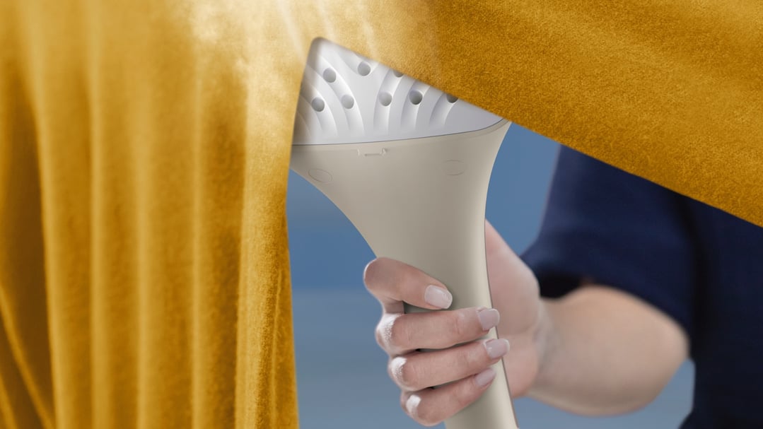 Hand holding a Philips Garment Steamer to a yellow garment
