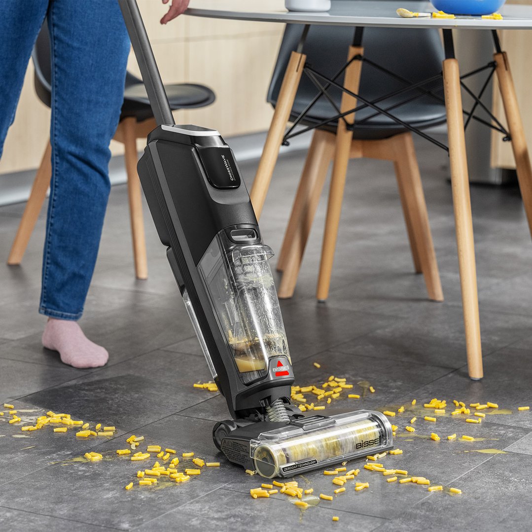 Person cleaning spilled macaroni and cheese from a kitchen floor with a vacuum cleaner