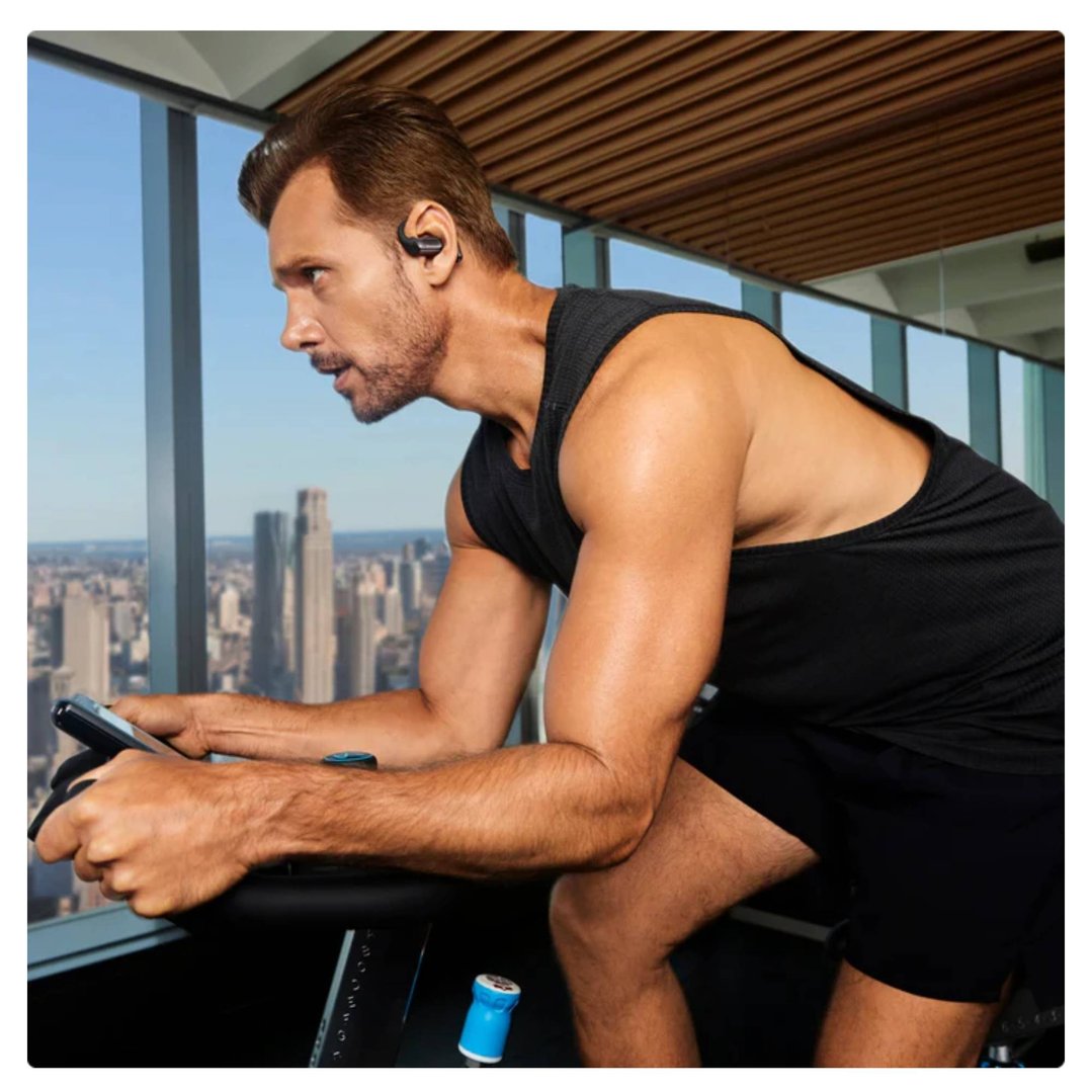 Man wearing black wireless headphones while cycling indoors with city view