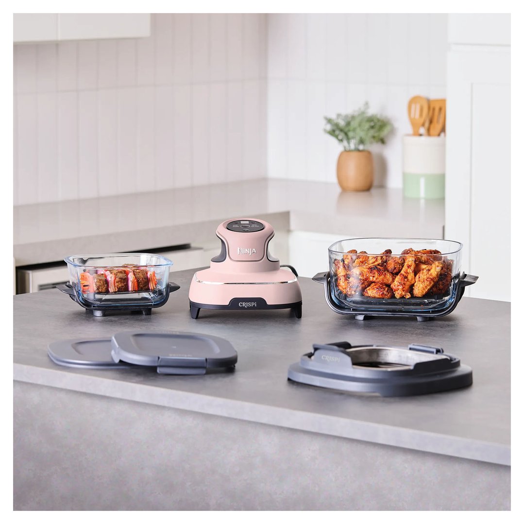 Pink Ninja Crispi air fryer on a kitchen counter with food in glass dishes
