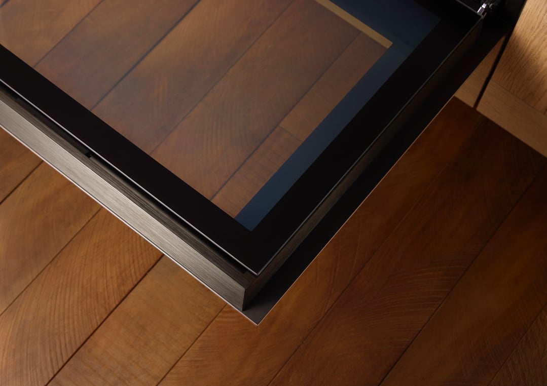Close up of a black oven door reflecting a wooden floor