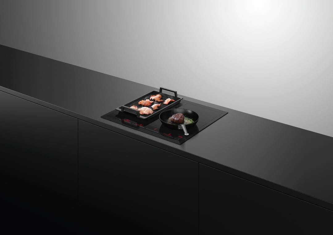 Induction cooktop with a grill pan and frying pan cooking food in a modern kitchen