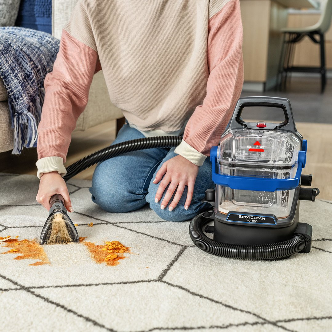 Person cleaning a spill on a white rug with a BISSELL SpotClean Turbo vacuum cleaner