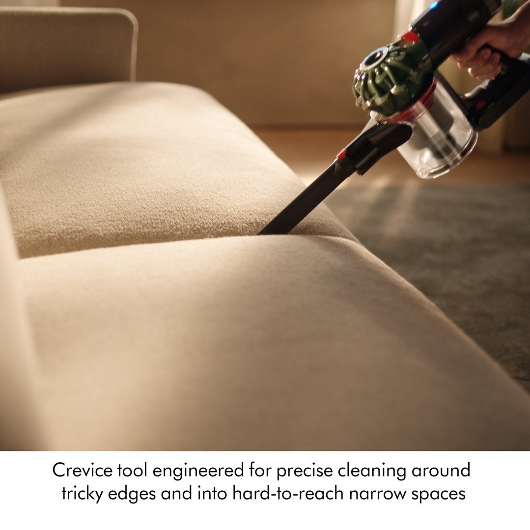 Hand using a Dyson V8 Cyclone Cordless Vacuum with crevice tool on a sofa