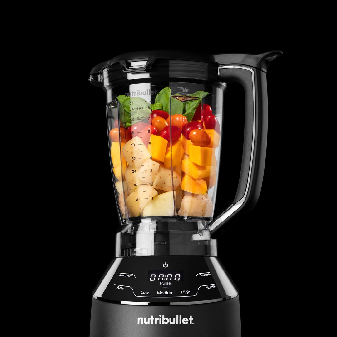 Black blender with vegetables and fruit inside on a black background