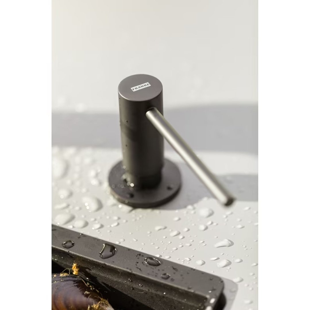 Matte black soap dispenser with a silver spout on a wet surface with mussels