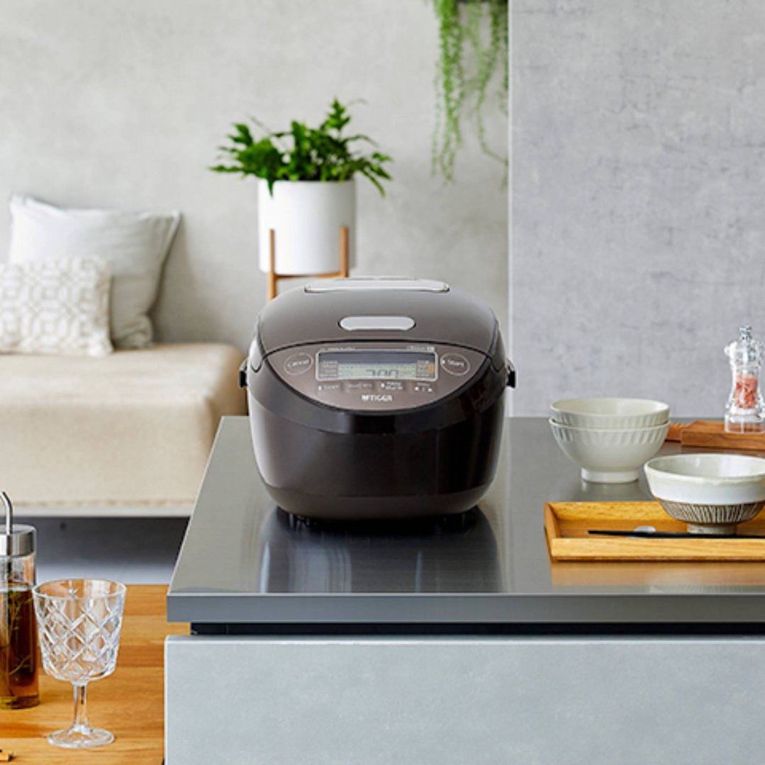 Tiger rice cooker on a kitchen counter with bowls and a plant in the background