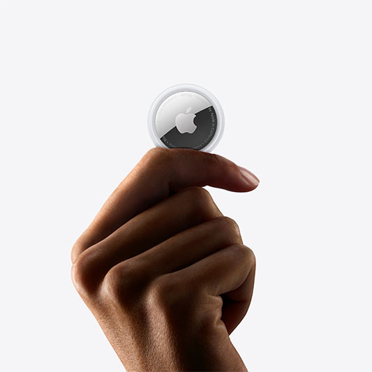 A hand holding an Apple AirTag between the thumb and index finger