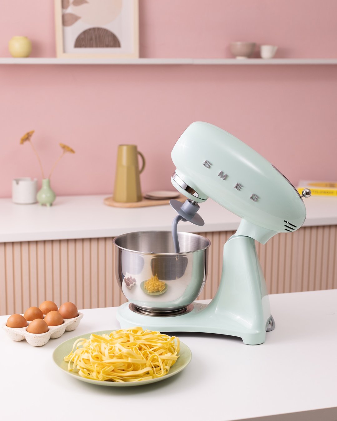 Pastel green stand mixer with bowl, eggs, and pasta on a kitchen counter