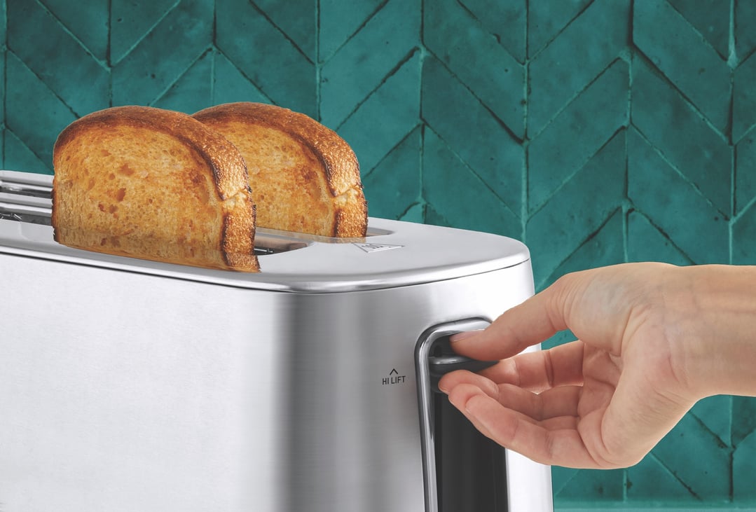 Hand pushing down lever of a toaster with two slices of toast