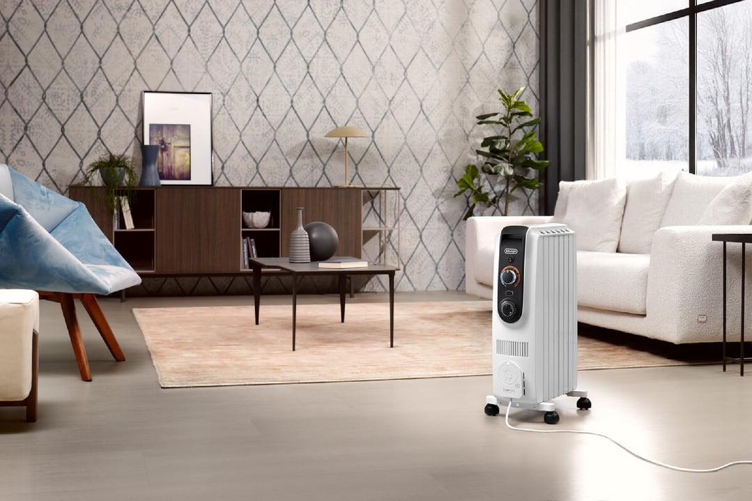 White oil column heater in a living room with a sofa and window view