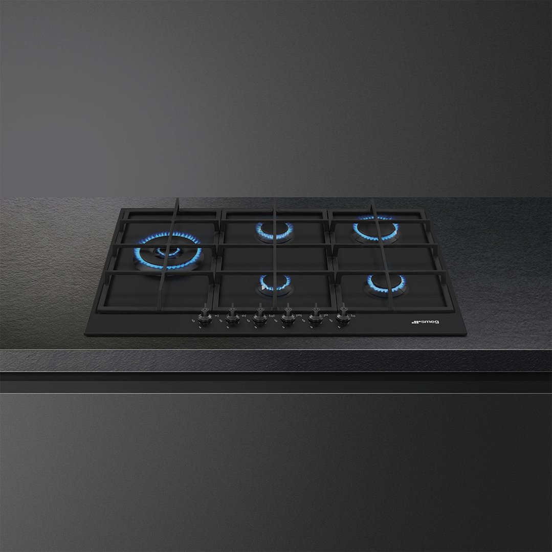 Black gas cooktop with five burners and blue flames on a dark countertop
