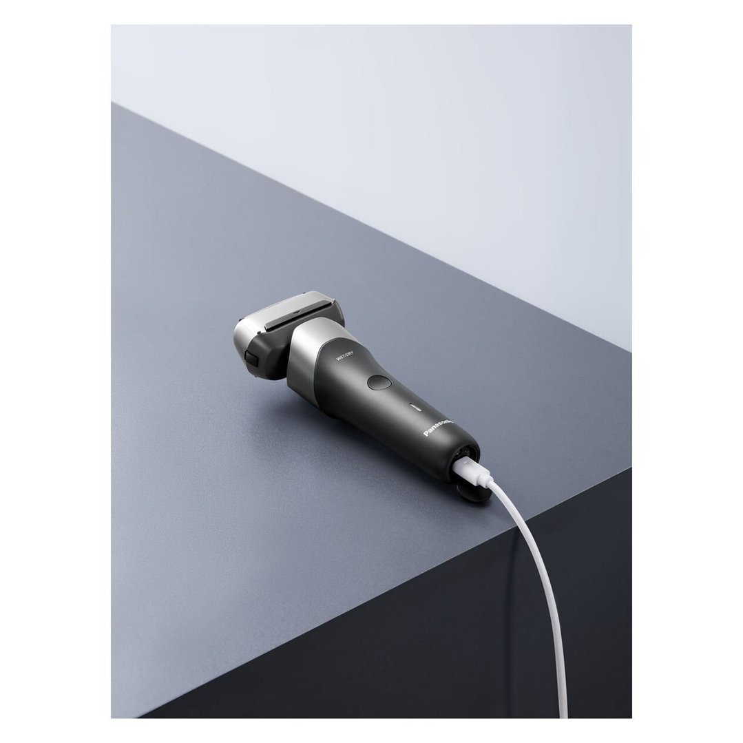 Black Panasonic electric shaver charging on a two-tone grey surface