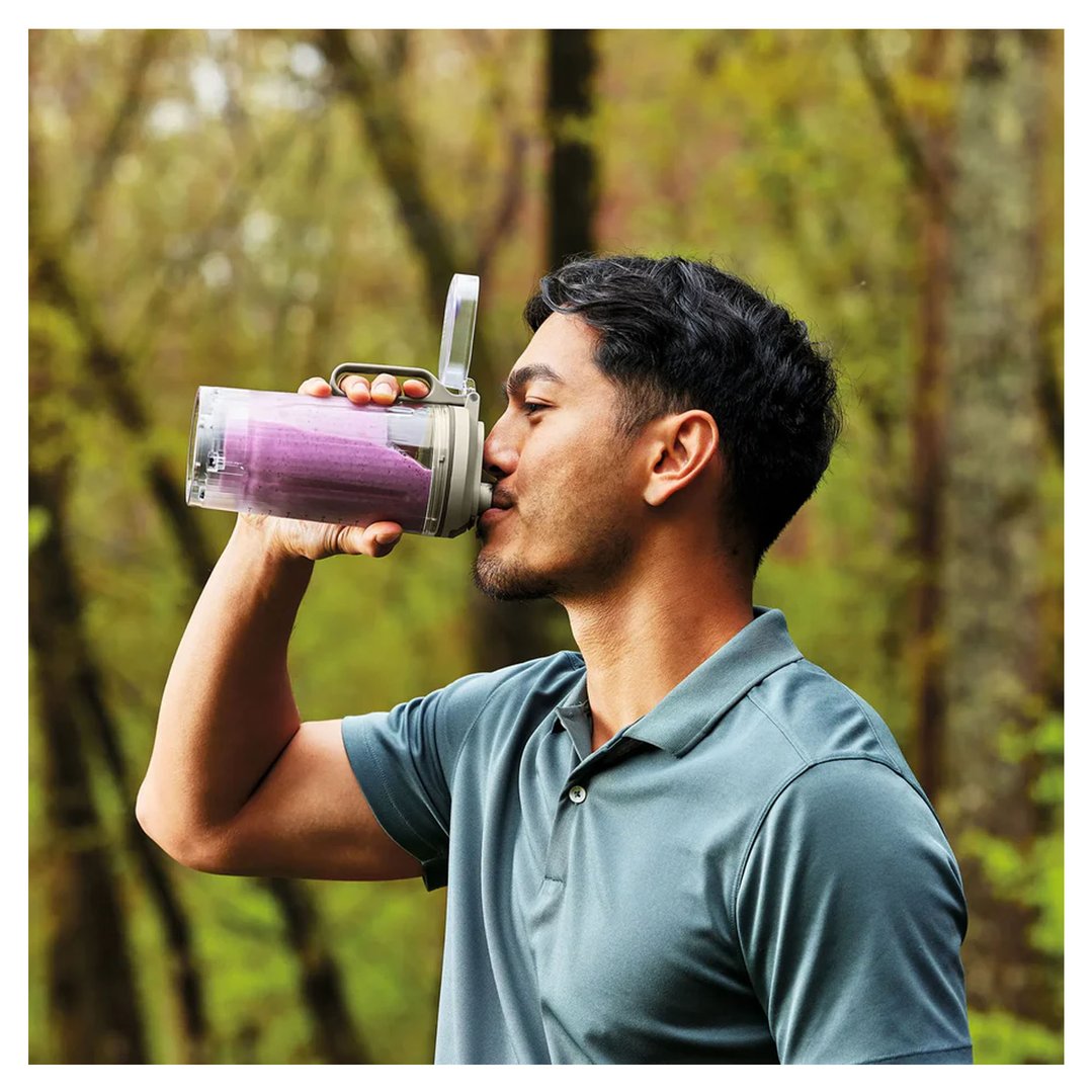Man drinking a purple smoothie from a portable blender outdoors