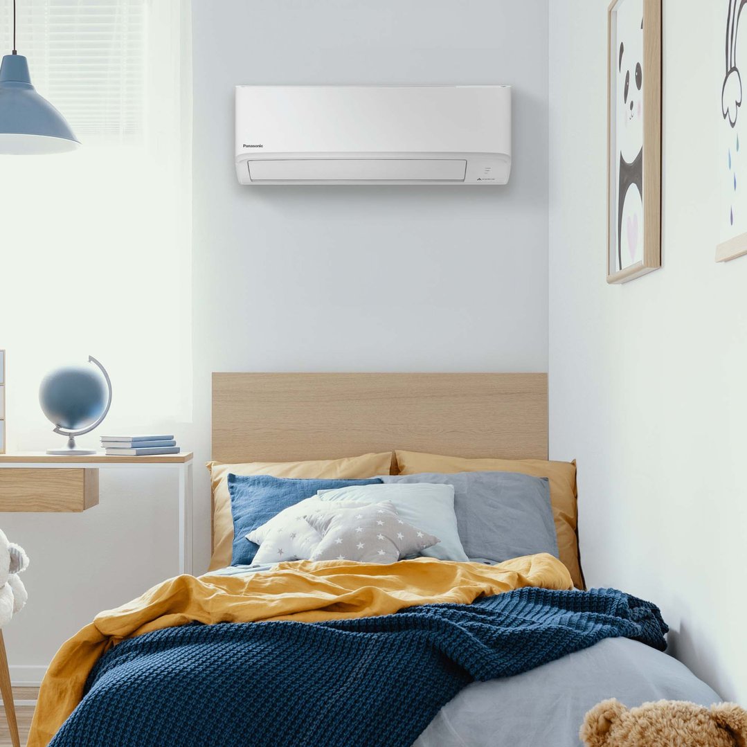 Panasonic air conditioner mounted on a white wall above a bed in a bedroom