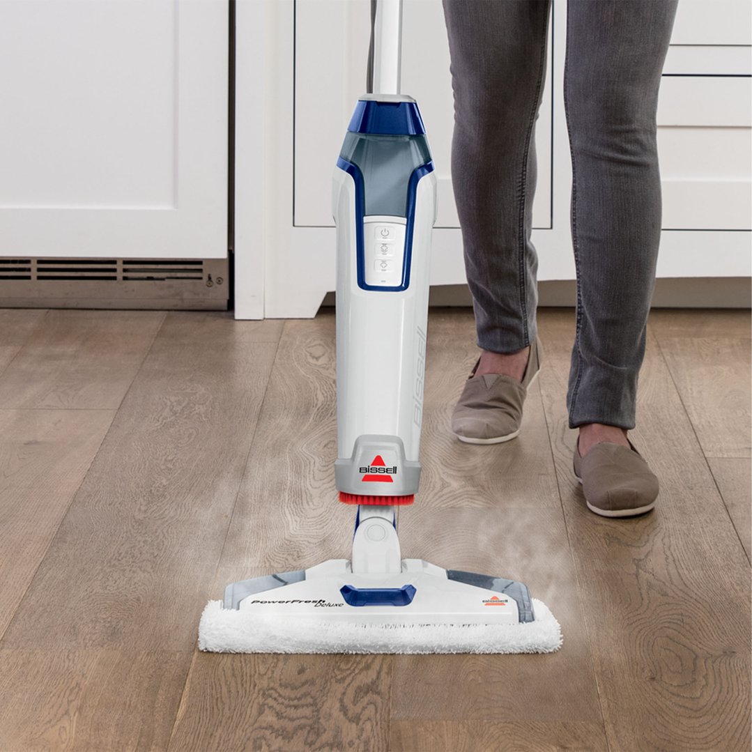 Person using a white BISSELL PowerFresh Deluxe steam mop on a wooden floor