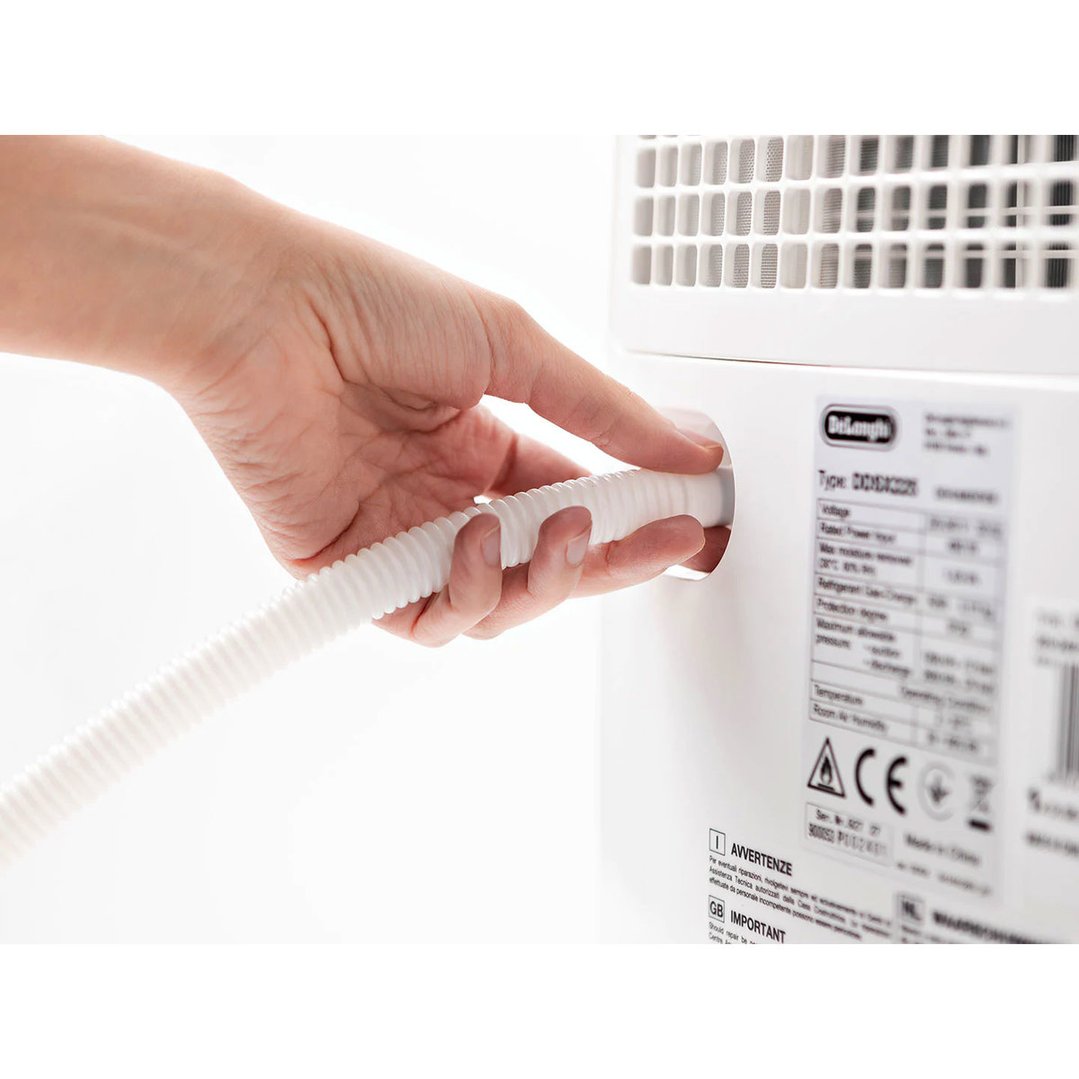 Hand inserting a white corrugated hose into the back of a De'Longhi dehumidifier