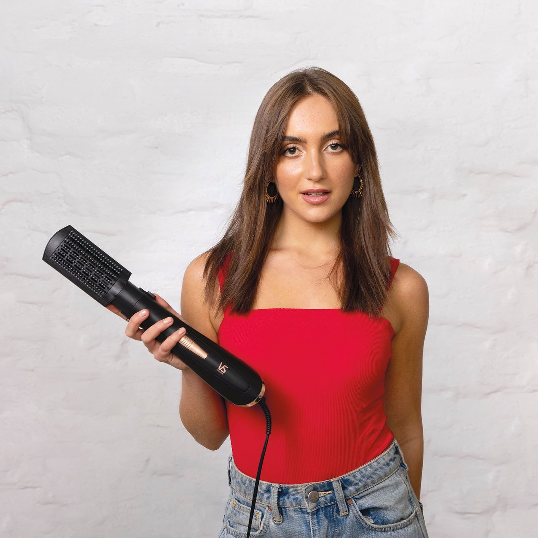 Woman in a red top and jeans holding a black hair styler