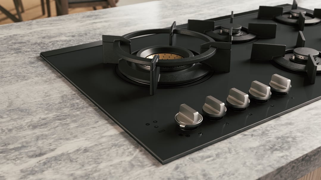 Close up of a black gas cooktop with five burners built into a stone benchtop