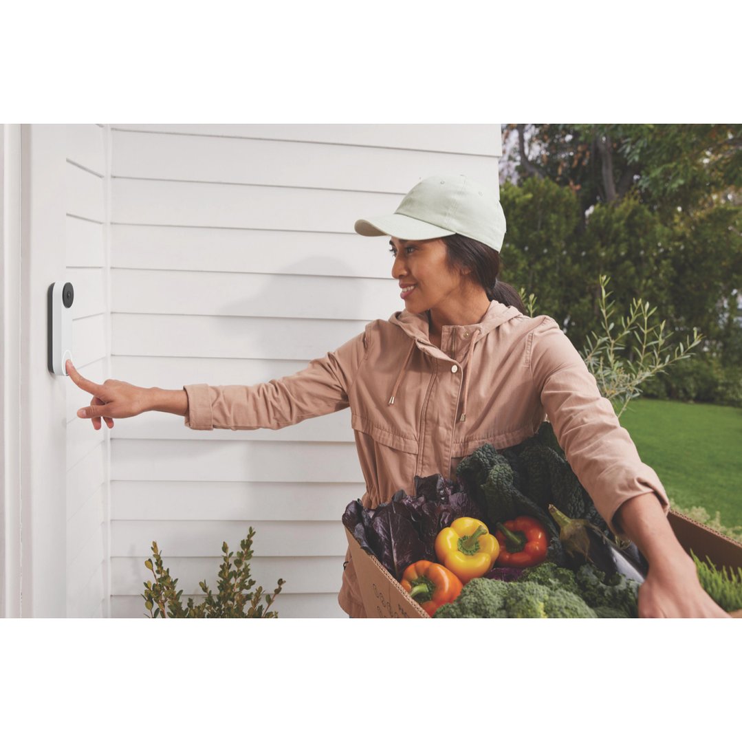 Woman pressing the Nest Doorbell (Battery) while holding a box of groceries