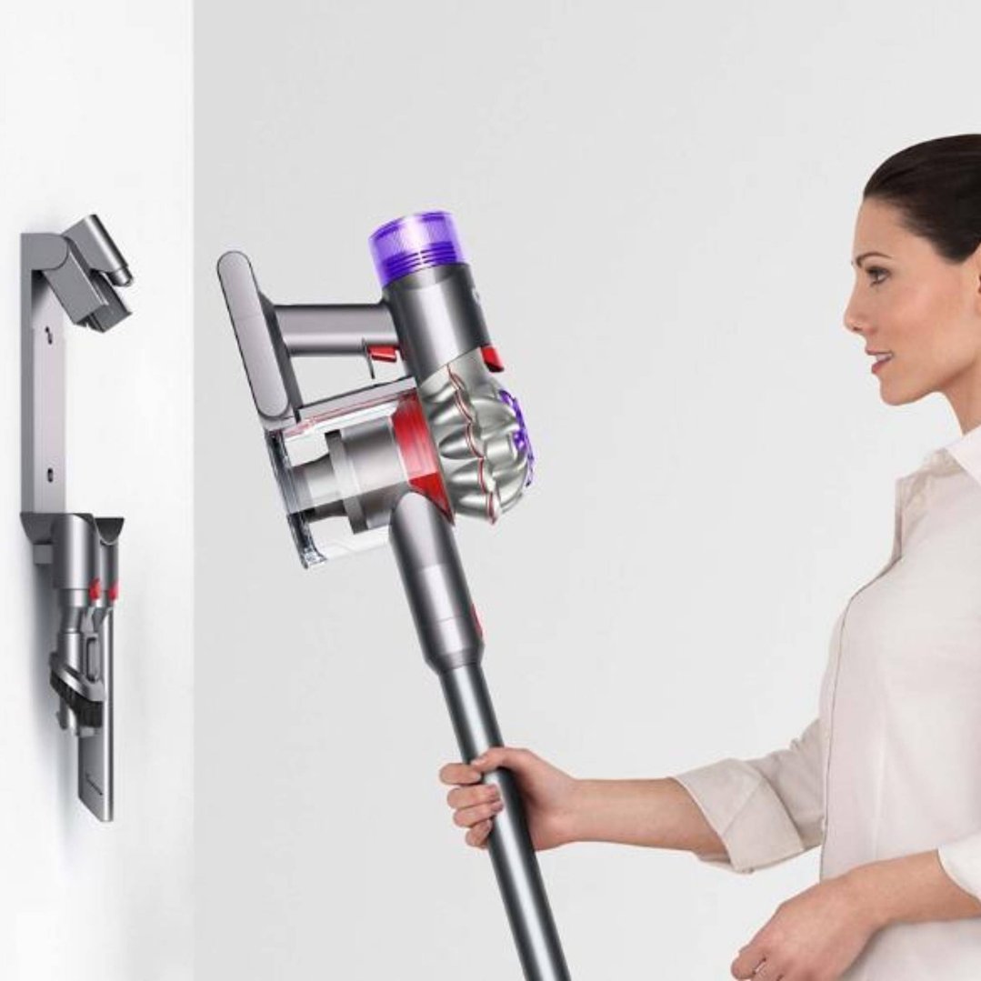 Woman holding a Dyson V8 Advanced Vacuum, with wall-mounted accessories in background