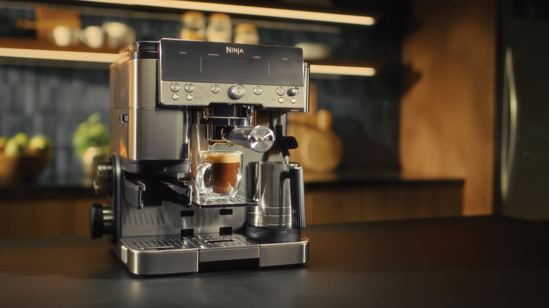 Ninja espresso machine brewing coffee into a glass mug on a kitchen counter