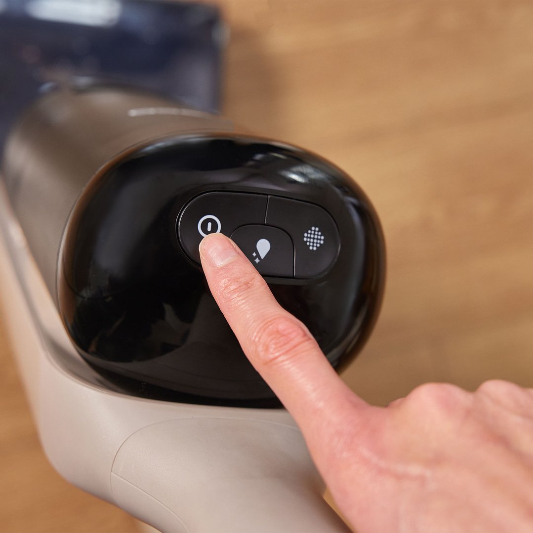 A finger pressing the power button on a black Tineco vacuum cleaner