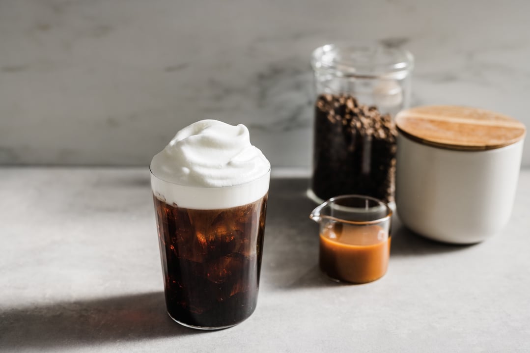 Iced coffee with foam, coffee beans, and caramel sauce on a counter